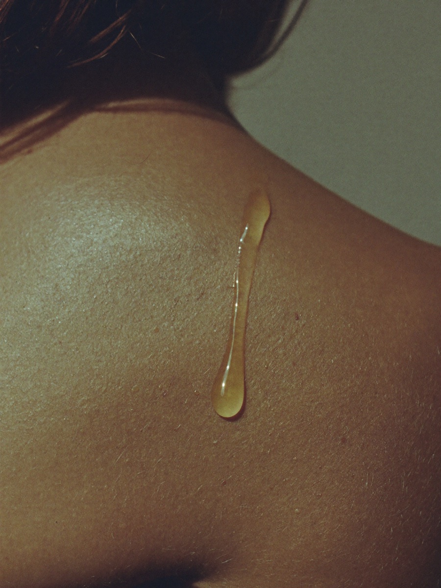 A single golden droplet of oil resting on skin, macro